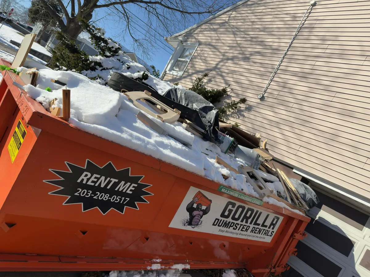 Dumpster filled significantly above the rim with household waste and trash bags